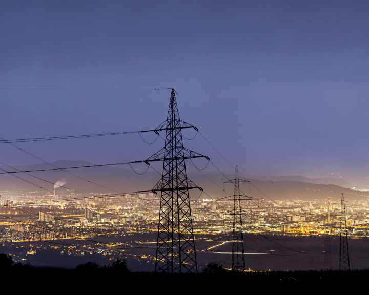 Imagem panoramica de uma cidade iluminada, com postes de alta voltagem em primeiro plano.