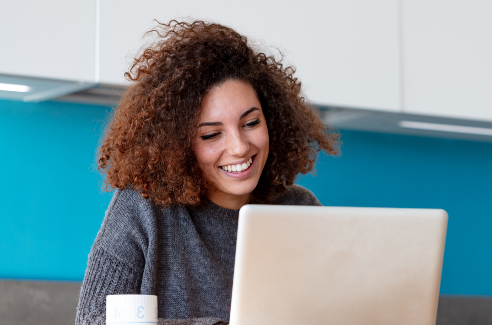 Mulher sentada mexendo em um notebook e sorrindo.